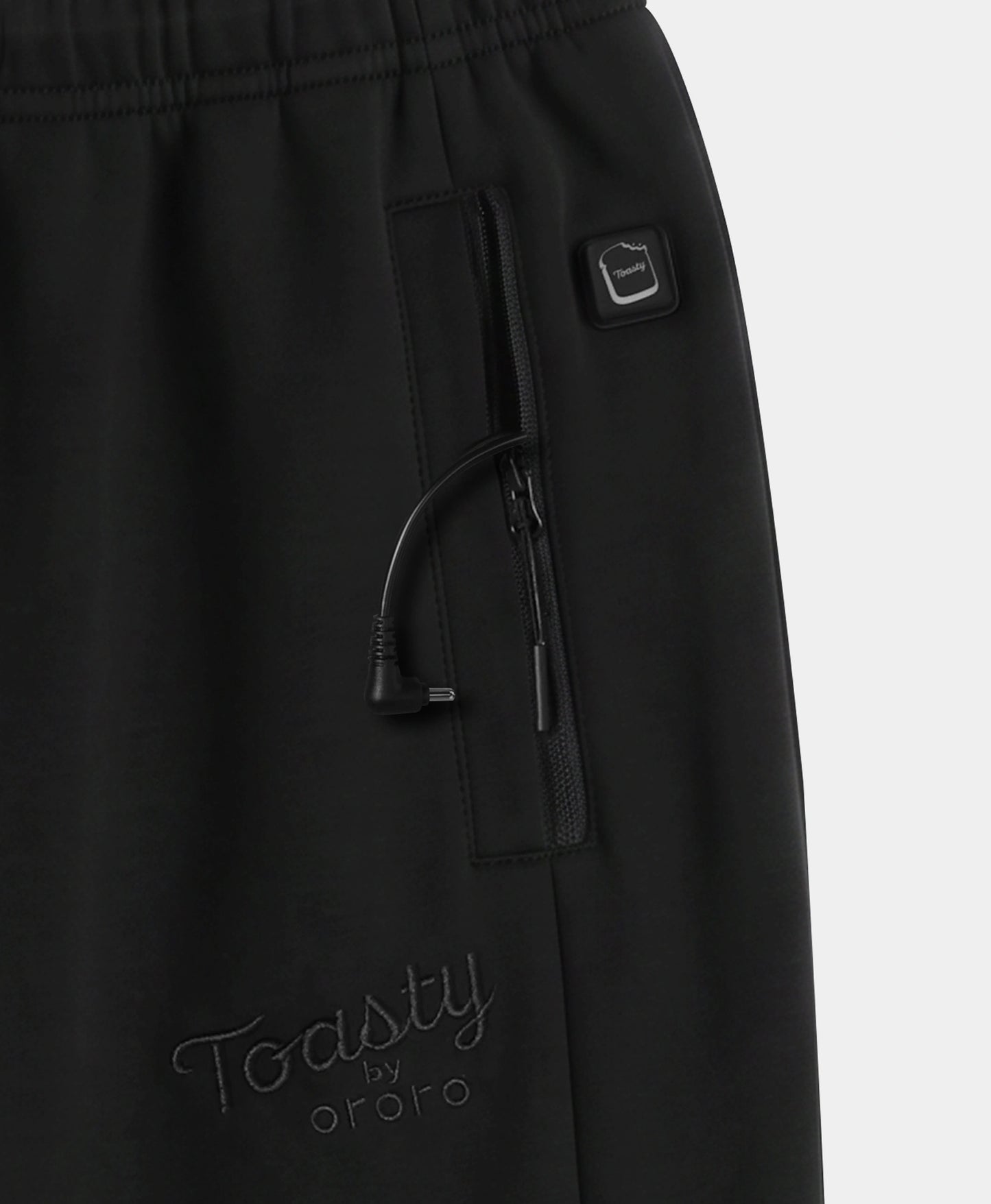 Close-up of black pants showing a side zip pocket with a drawstring, a small square logo tab, and tonal embroidered 'Toasty by ororo' branding near the lower left leg.
