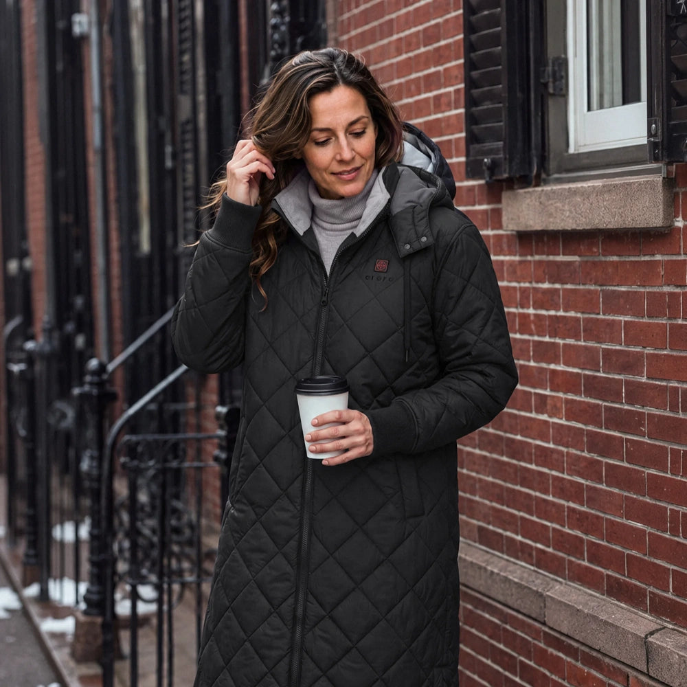 Uptown Women's 4-Zone Heated Parka in black, worn with hood while holding coffee outdoors
