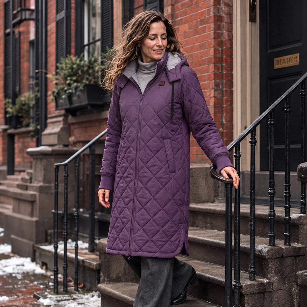 Uptown Women's 4-Zone Heated Parka in black, worn while walking with coffee on a snowy city