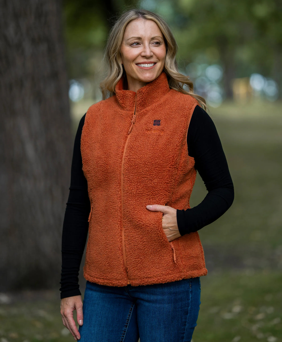 A woman standing outdoors in a park wearing ororo Heated Recycled Fleece Vest