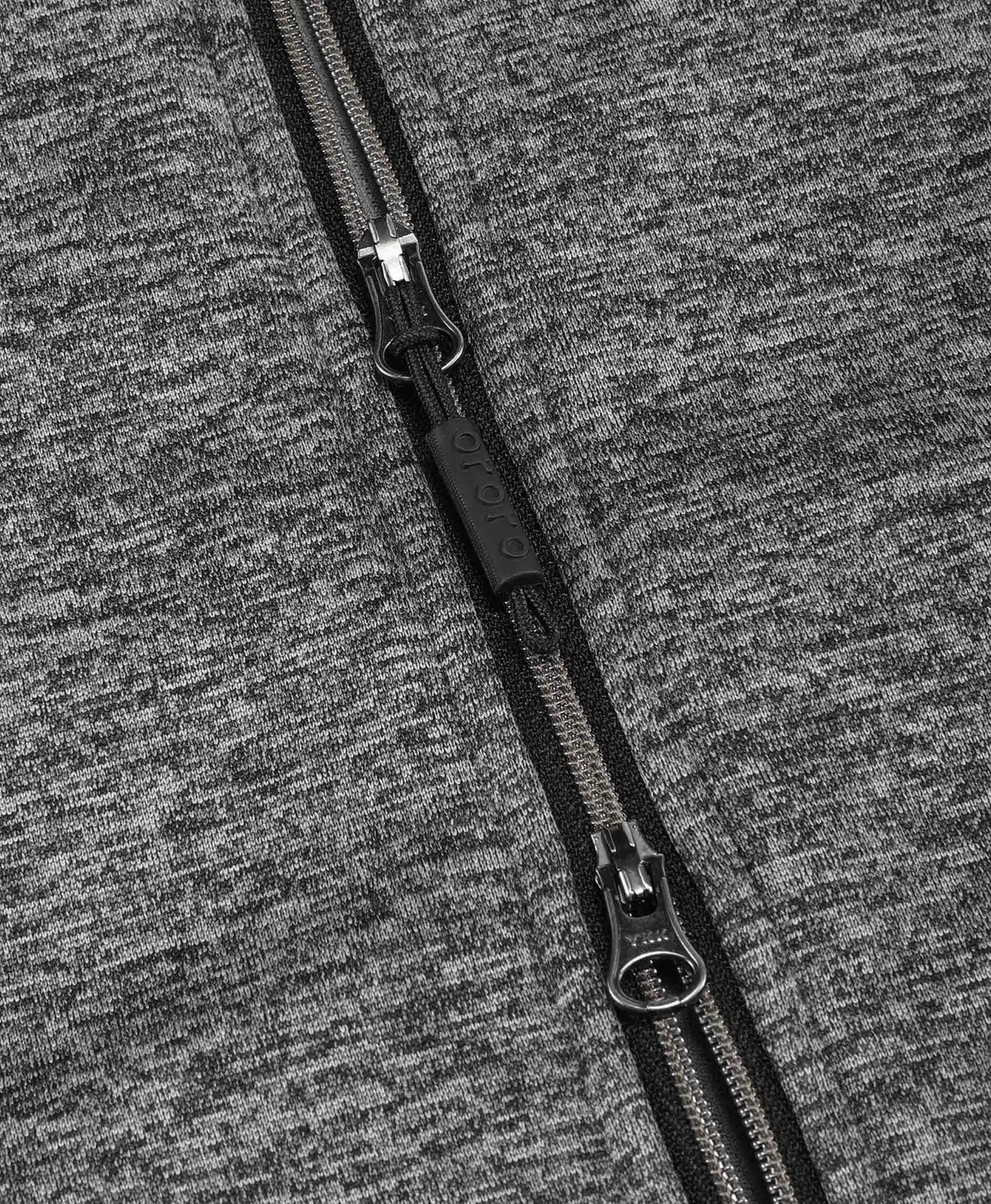 Close-up of a black zipper with a black pull tab on a heather gray fabric surface.