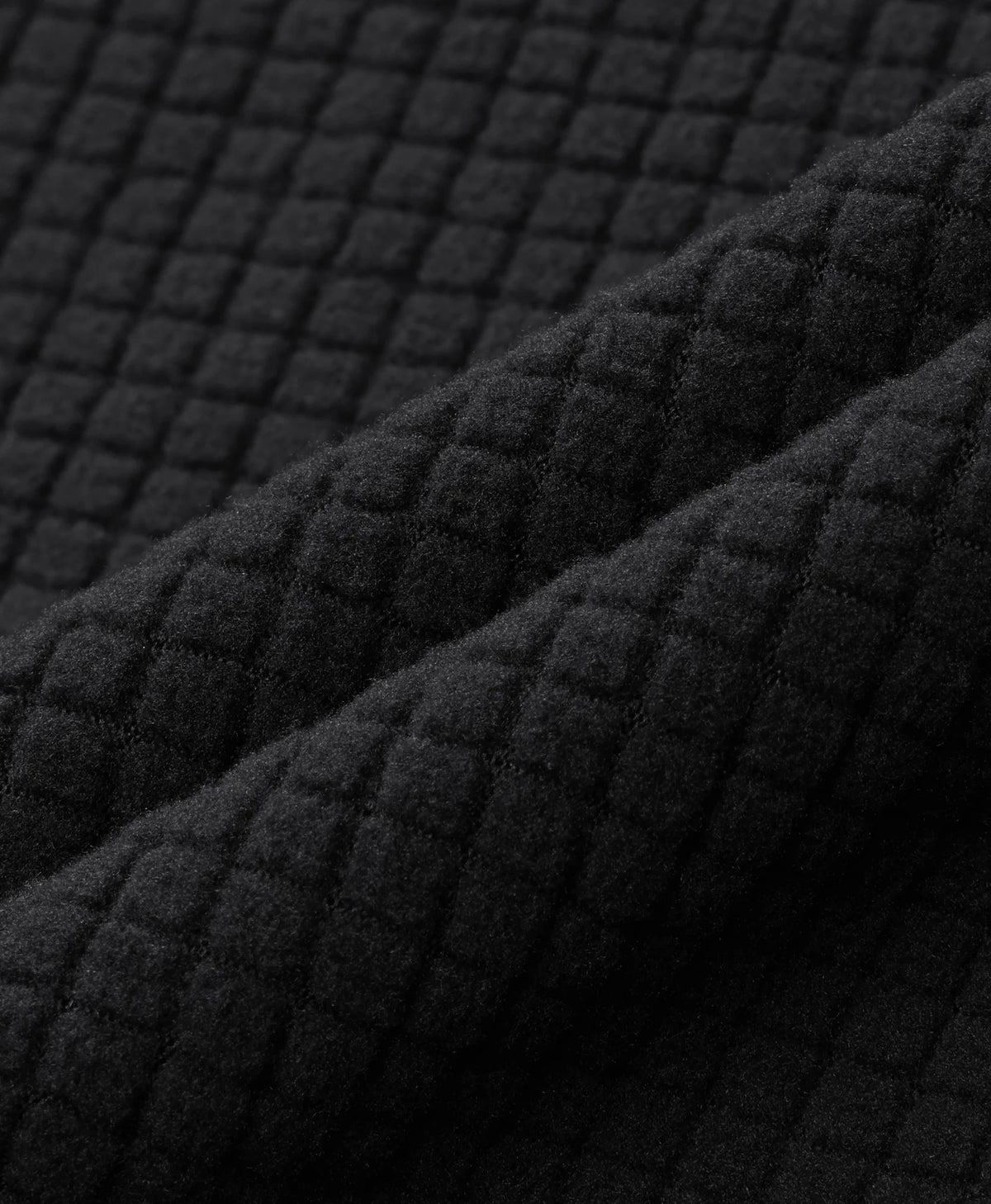 Close-up of a black quilted fabric with a textured diamond pattern, shown in soft folds.