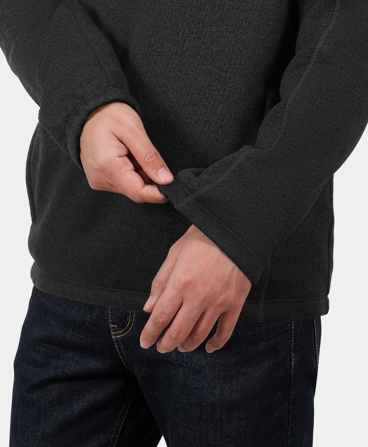 A person wearing a black ribbed knit sweater and dark blue jeans, showing the ribbed texture and cuff detail.