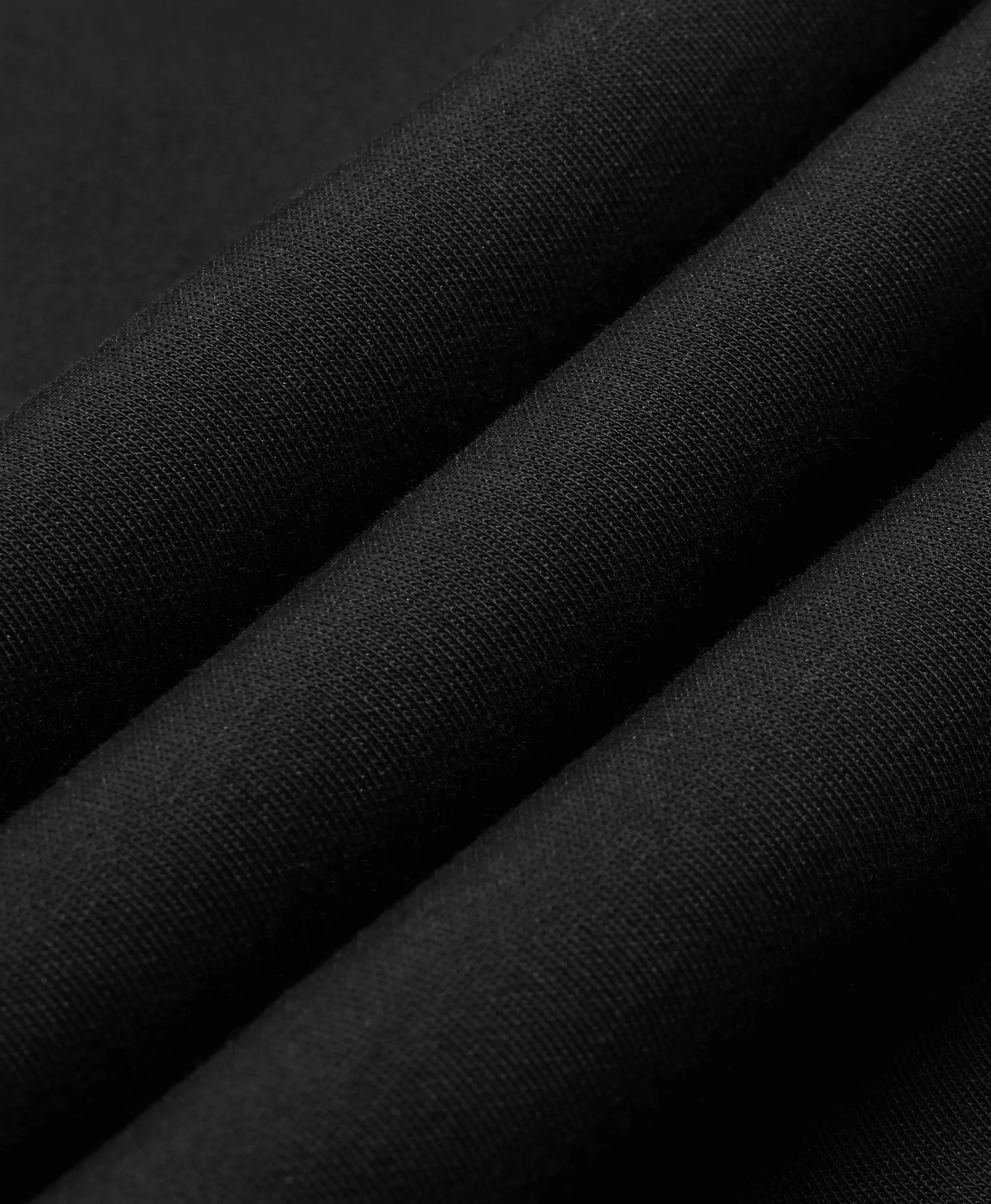 A black Toasty Unisex 5-Zone Heated Pullover Hoodie, displayed in a macro close-up of draped black fabric with soft diagonal folds showing a fine woven texture.