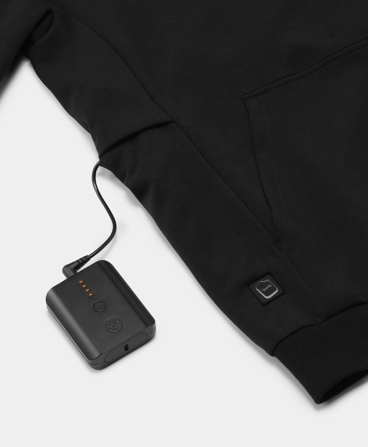 A black Toasty Unisex 5-Zone Heated Pullover Hoodie, displaying a close-up of the illuminated power button near the bottom hem, connected to a portable rechargeable battery stored in the exterior battery pocket on the right side.