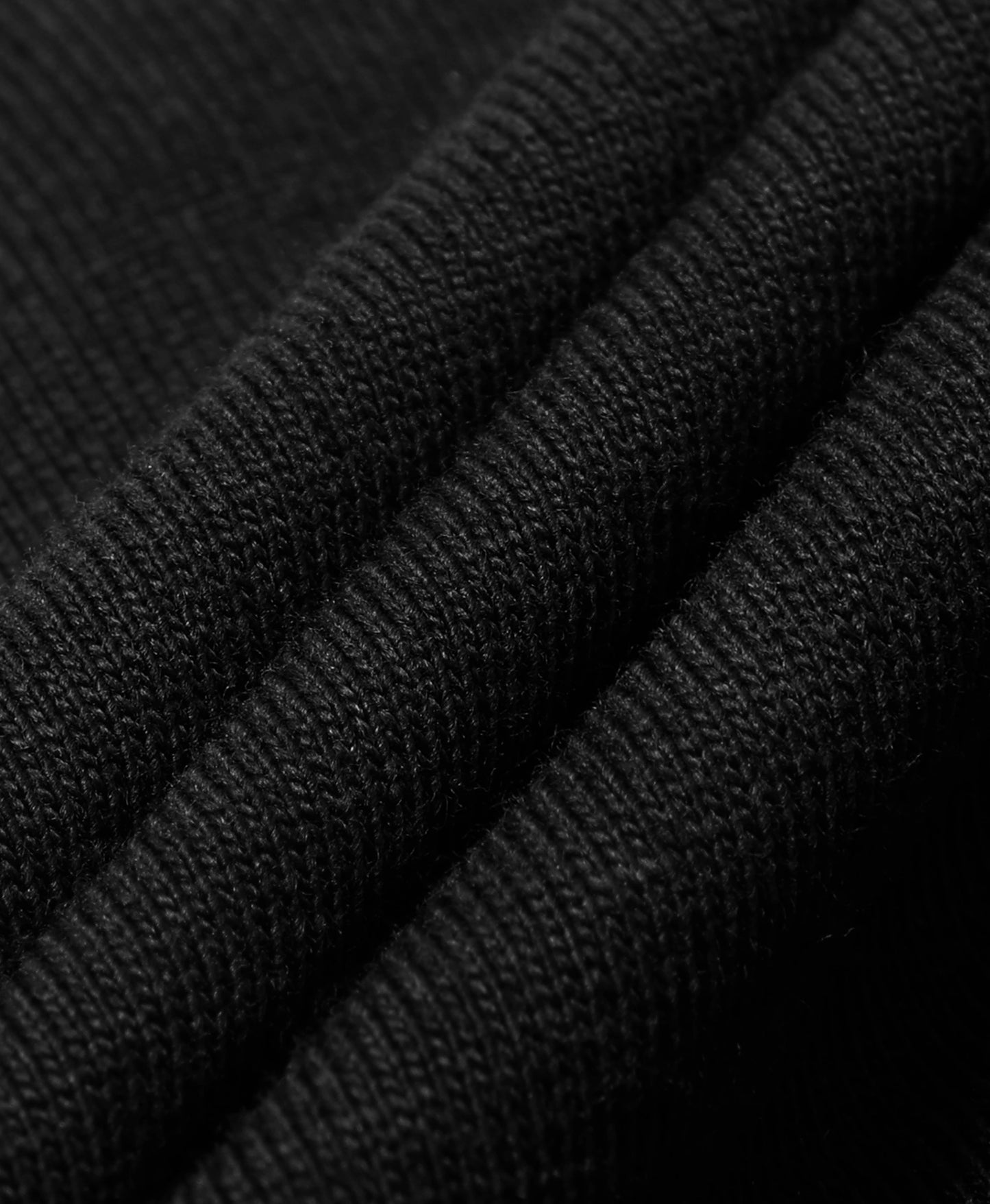 A close-up of black ribbed knit fabric with soft diagonal folds showing the texture and weave.