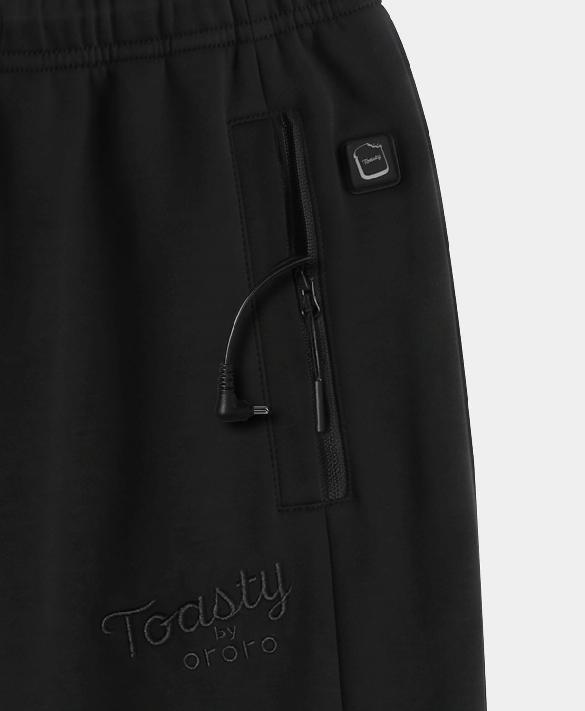 Close-up of black pants showing a side zip pocket with a drawstring, a small square logo tab, and tonal embroidered 'Toasty by ororo' branding near the lower left leg.