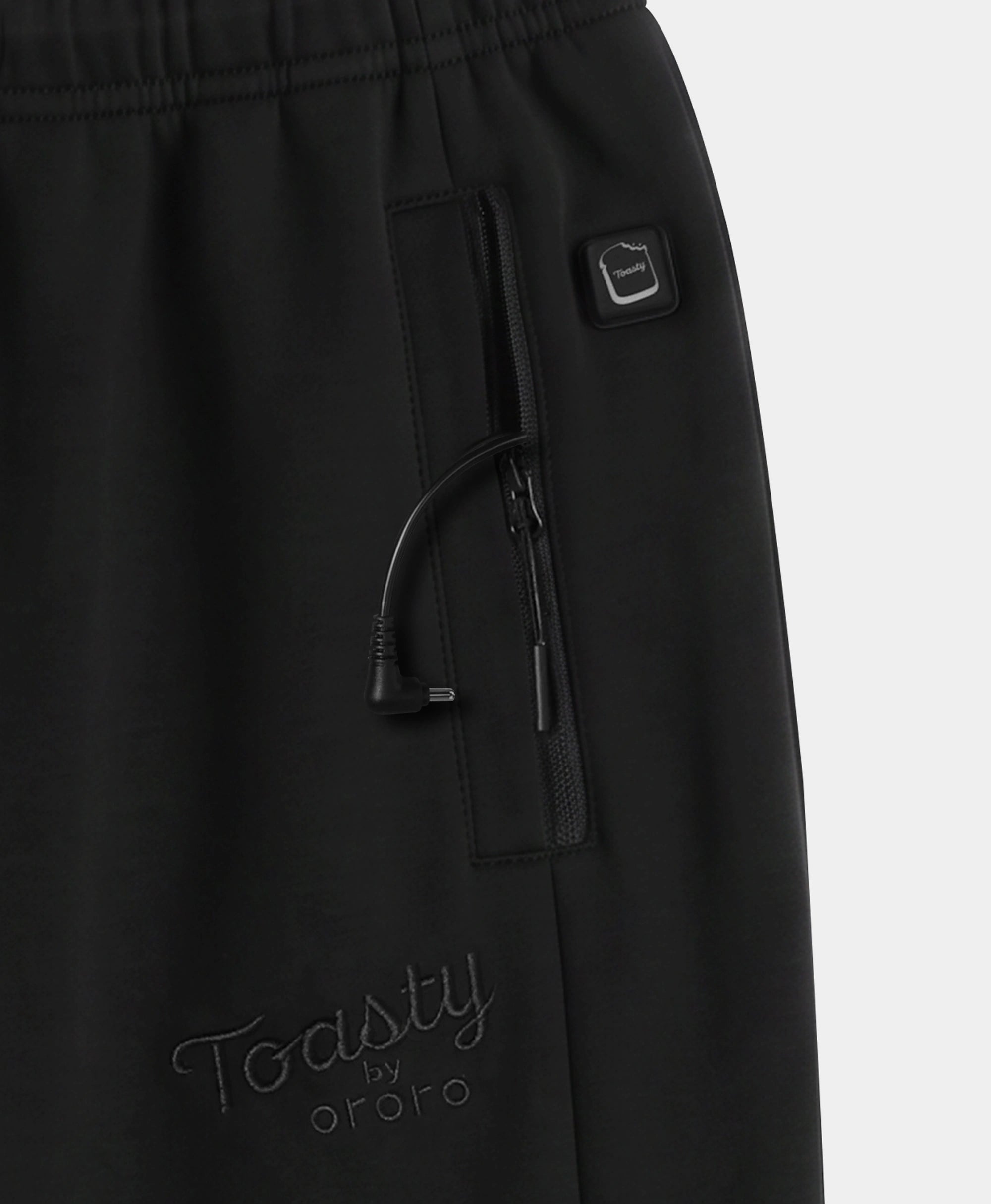 Close-up of black pants showing a side zip pocket with a drawstring, a small square logo tab, and tonal embroidered 'Toasty by ororo' branding near the lower left leg.